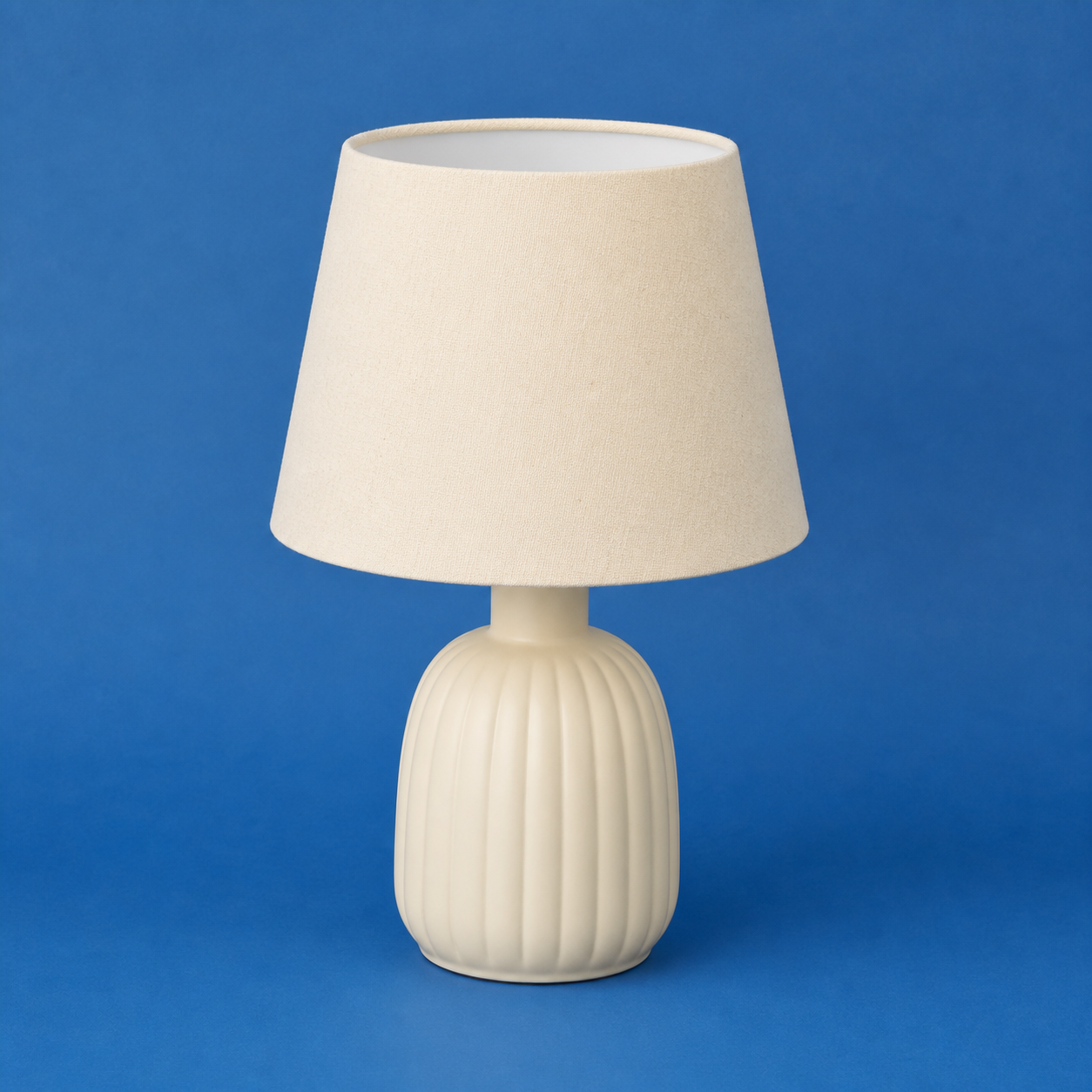 Original demonstration photograph of a pale table lamp on a matte blue backdrop